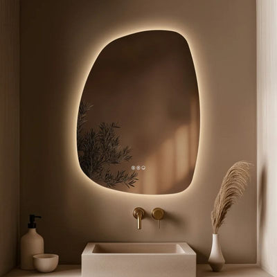 The Origins Living Claris illuminated mirror collection - image shows an organic shaped mirror with warm LED back lighting in a modern beige bathroom setting.